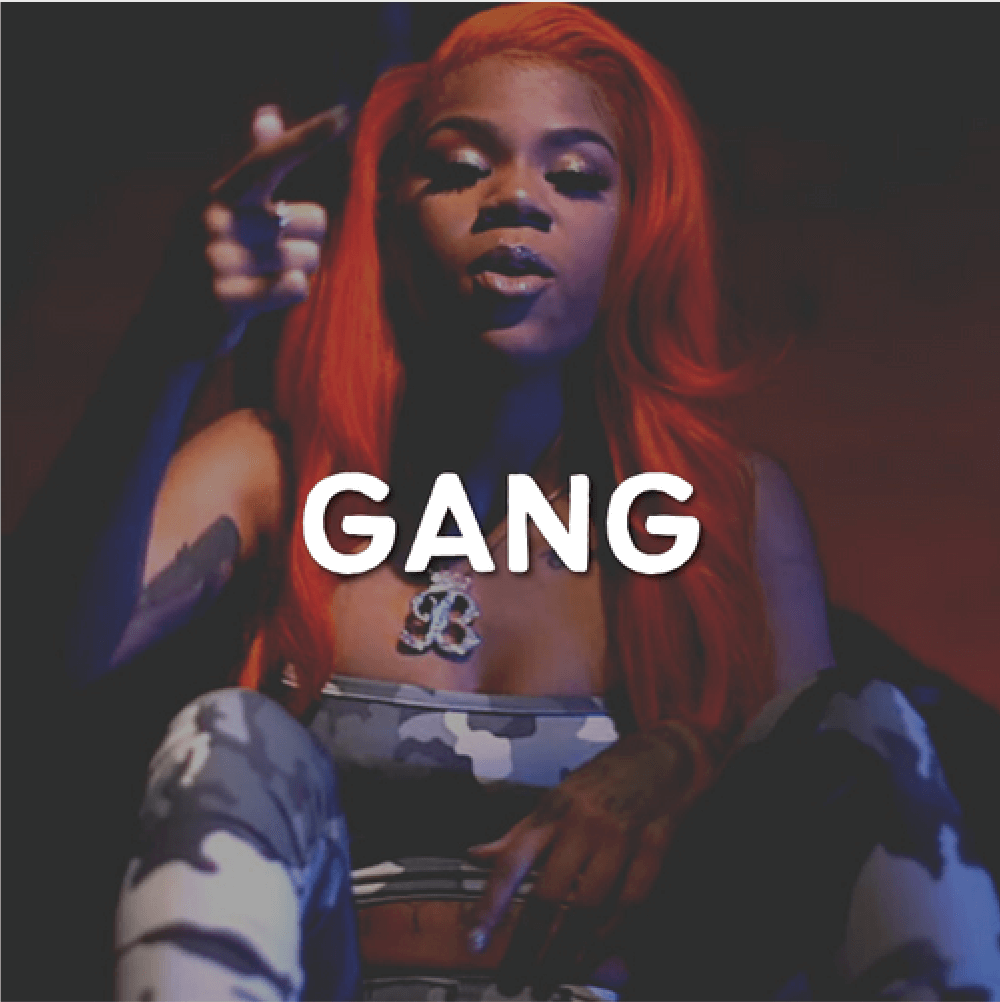 A person with long red hair sits confidently, wearing a strapless top and camouflage pants. Adorned with tattoos and a large pendant necklace, they effortlessly embody the essence of "Gang," making it resonate boldly across the image.