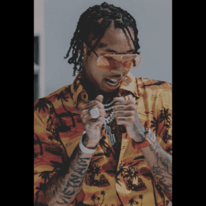 A person with braided hair, wearing orange-tinted glasses and a colorful floral shirt, strikes an energetic pose. They accessorize with stunning pieces from the Diamonds collection, including diamond-studded necklaces and rings, proudly displaying tattoos on both arms against a muted gray background.